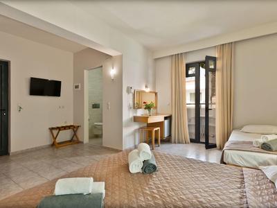 Brightly furnished hotel room with double bed, single bed, desk, and TV on the wall.