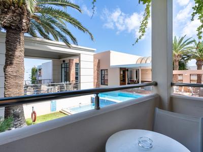 Modern balcony with table overlooking a pool and palm trees on a sunny day.