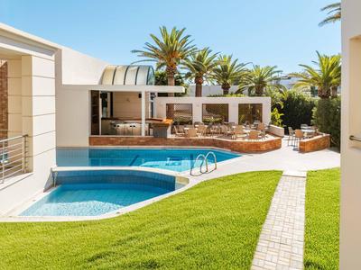 Moderner Außenpool mit Liegestühlen und Palmen in einer Hotelanlage bei Sonnenschein.