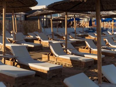 Empty lounge chairs with sun umbrellas on sandy beach at sunset.