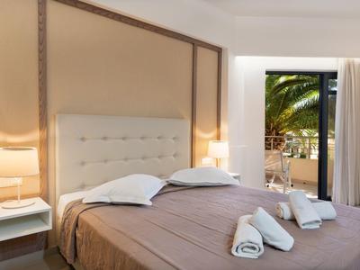 Brightly furnished bedroom with double bed and view of a balcony with palm trees.