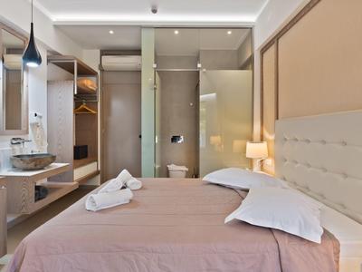 Modern hotel room with double bed, open wardrobe, and integrated bathroom.