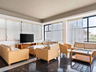 Bright hotel lounge with leather armchairs, sofas, tables, and large windows overlooking outside.