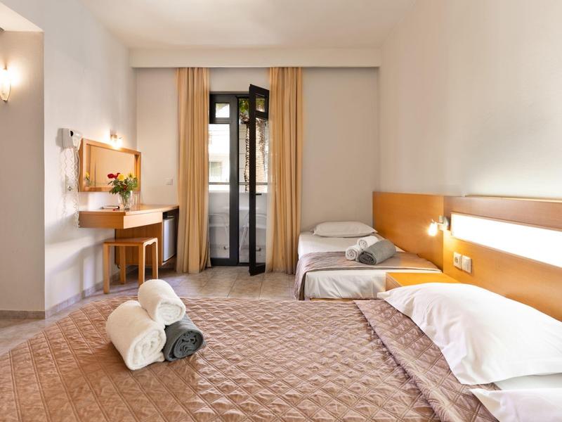 Bright hotel room with double bed, two single beds, and balcony view.