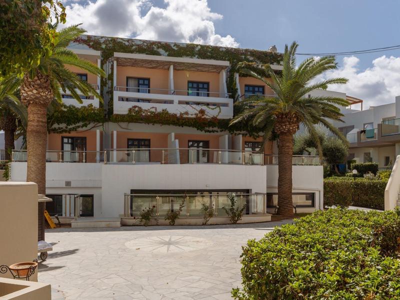 Multi-story hotel with balconies, palm trees, and fenced outdoor swimming pool.