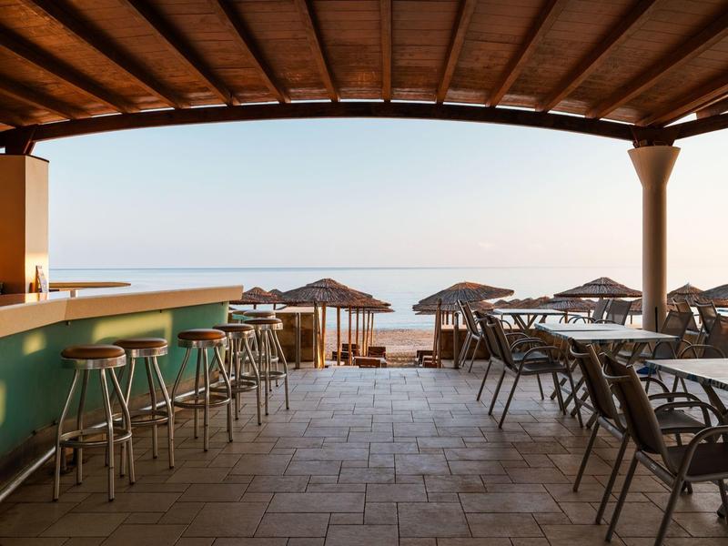 Open beach bar with stools and umbrellas, view of calm sea at sunset.