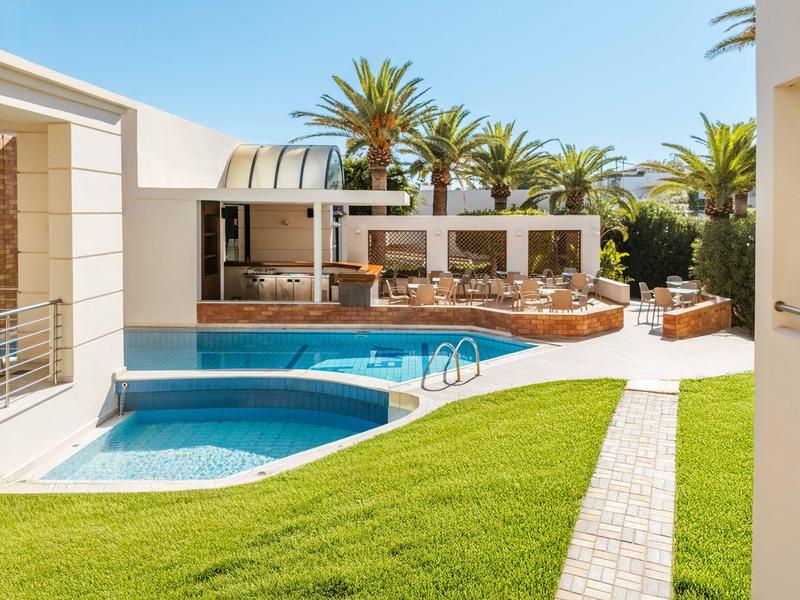 Modern outdoor pool with sun loungers and palm trees at a hotel on a sunny day.
