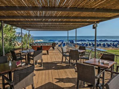 Terrasse couverte avec sièges et vue sur une plage avec parasols et la mer.