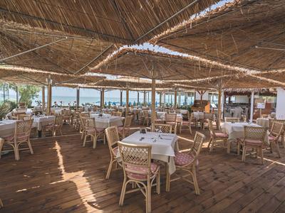 Grande ristorante coperto con pavimento in legno e molti tavoli apparecchiati vicino al mare.