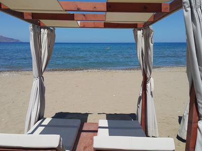 Deux chaises longues sous une cabane couverte sur une plage de sable avec vue sur la mer.