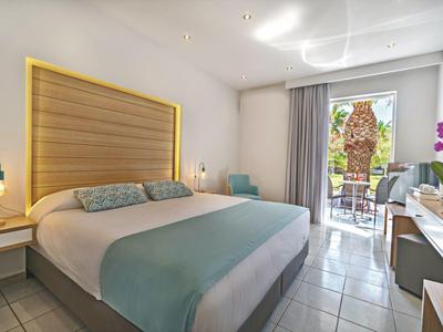 Chambre d'hôtel moderne avec grand lit, bureau, balcon et vue sur le jardin.