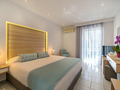 Chambre d'hôtel lumineuse avec lit double, tête de lit en bois moderne et accès au balcon ou à la terrasse.