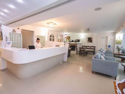 Lobby dell'hotel luminosa con banco reception bianco, area salotto e tavolo da pranzo sullo sfondo.