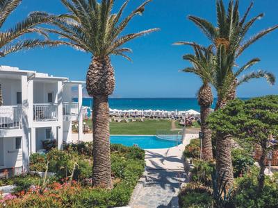 Vue d'un hôtel avec piscine, palmiers et mer en arrière-plan sous un ciel bleu clair