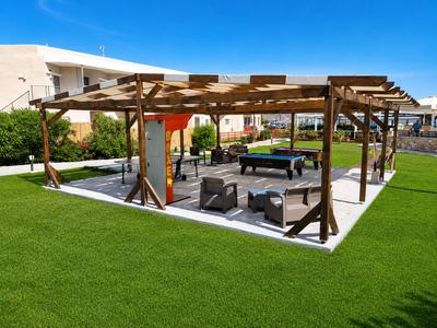 Espace jardin ouvert avec toiture en bois, sièges et billard sur pelouse soignée.