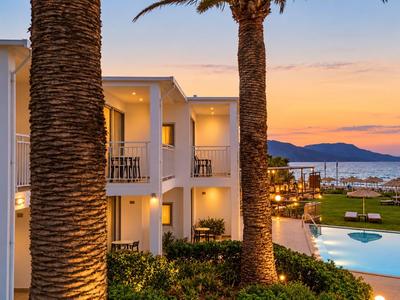 Hotel moderno con piscina y palmeras junto al mar al atardecer.