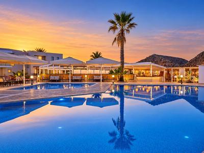 Piscine d'hôtel au coucher du soleil avec des palmiers et des bâtiments éclairés en arrière-plan.