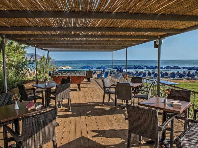 Terrasse couverte avec sièges et vue sur une plage avec parasols et la mer.