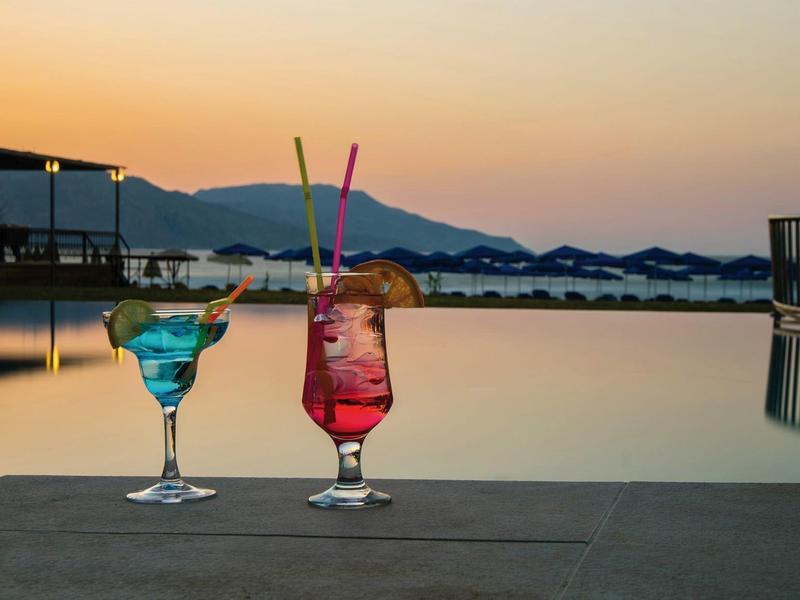Deux cocktails colorés au bord d'une piscine au coucher du soleil avec des montagnes en arrière-plan.