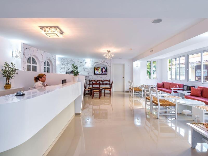 Réception d'hôtel lumineuse avec comptoir blanc, espace salon et grandes fenêtres.