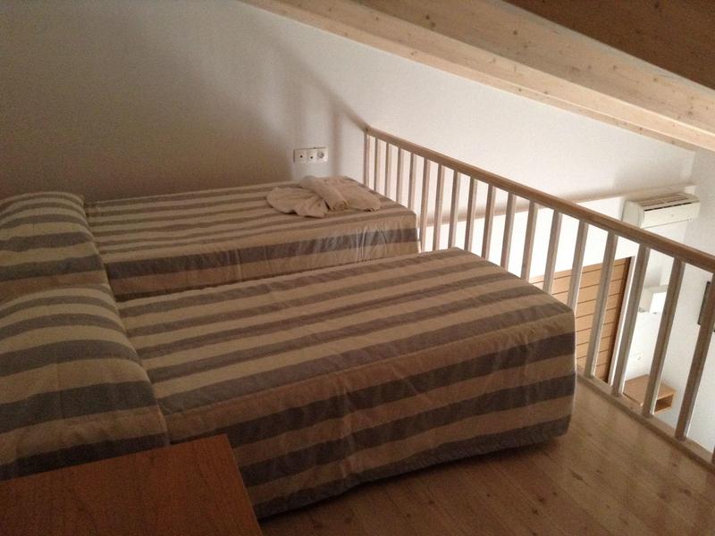 Deux lits avec des couvertures rayées dans une pièce lumineuse et ouverte avec un sol en bois et une rambarde.