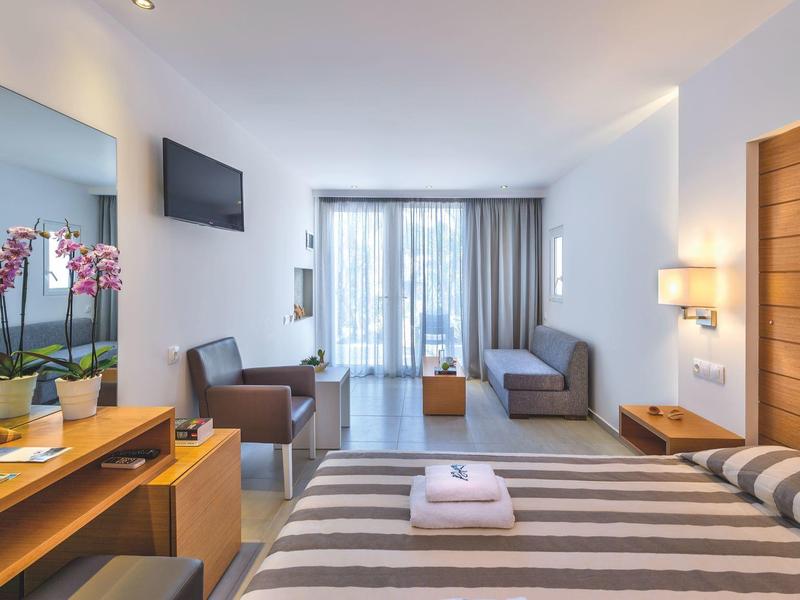 Chambre d'hôtel moderne avec lit double, canapé, bureau et balcon avec rideaux.