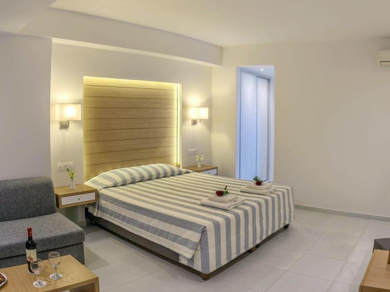 Chambre d'hôtel moderne avec lit double, canapé, bureau et design minimaliste aux couleurs neutres.