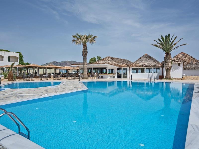 Grande piscine extérieure avec eau bleue claire et parasols devant des bâtiments sous un ciel bleu.