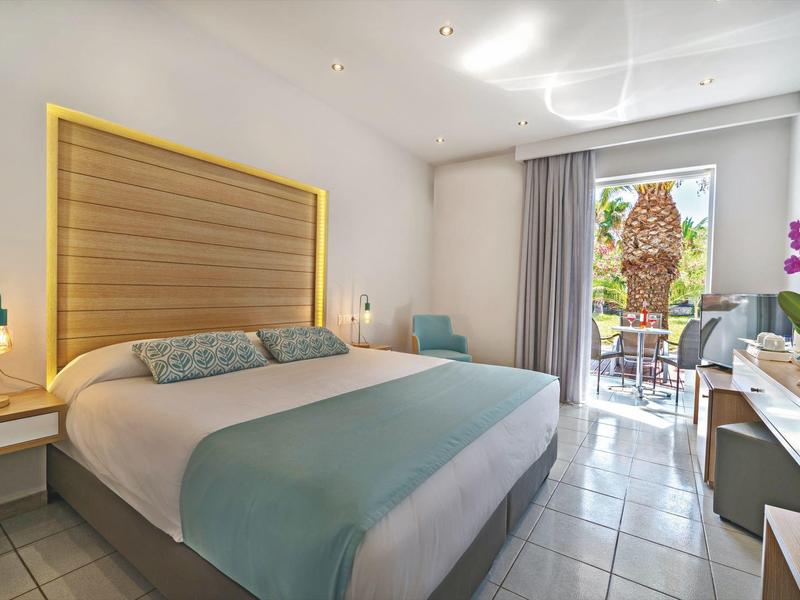 Chambre d'hôtel moderne avec grand lit, bureau, balcon et vue sur le jardin.