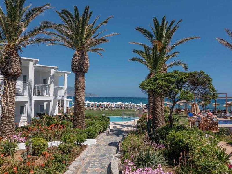 Chemin entre palmiers et fleurs menant à la mer avec des bâtiments d'hôtel blancs et des parasols