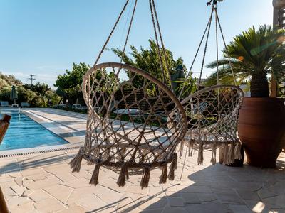 Sillas colgantes en una terraza con vista a la piscina y jardín bajo el sol.