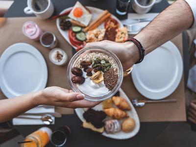 Due persone condividono una ciotola di cereali per colazione con vari ingredienti su un tavolo apparecchiato.