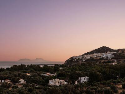 Vista di una città costiera al tramonto con montagne e mare sullo sfondo.