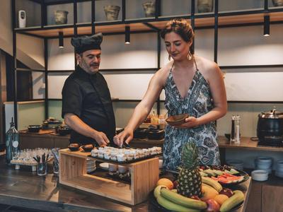 Mujer tomando comida de la parrilla en buffet en cocina de hotel con chef al fondo.