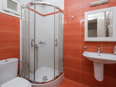 Bagno moderno con doccia curva, lavabo e WC, pareti piastrellate rosse.