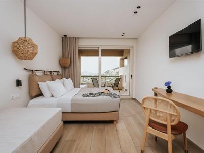 Habitación de hotel moderna con cama doble, TV, escritorio de madera y área de descanso con vista al balcón.