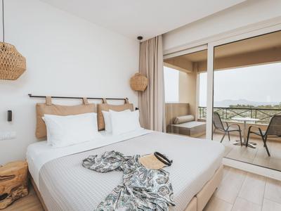 Habitación de hotel moderna con cama grande, cortinas claras y balcón con vista a las montañas.