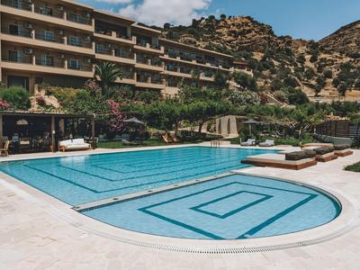 Piscina moderna con tumbonas frente a un edificio de hotel y paisaje rocoso de fondo.