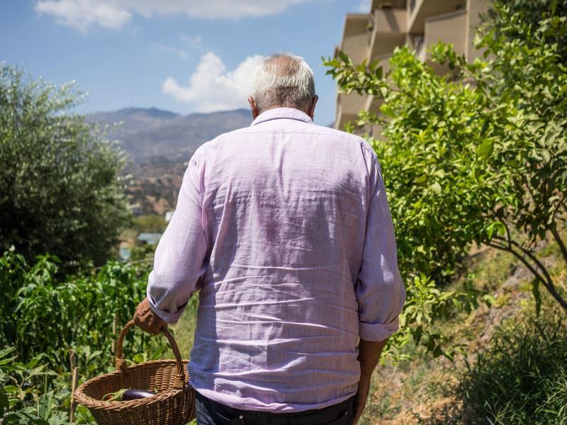 Uomo anziano con camicia chiara e cestino in giardino vicino a un edificio in una giornata di sole