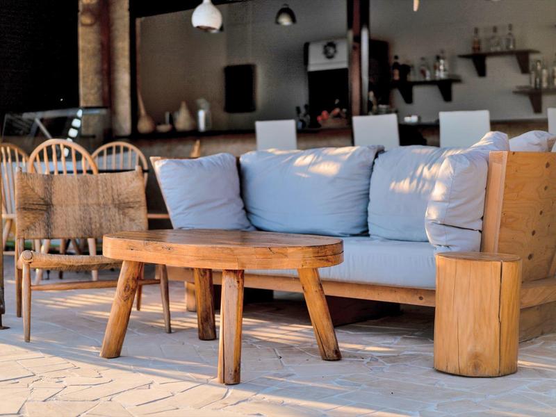 Accogliente zona lounge esterna con divano in legno, cuscini blu e tavolo in legno alla luce del giorno.