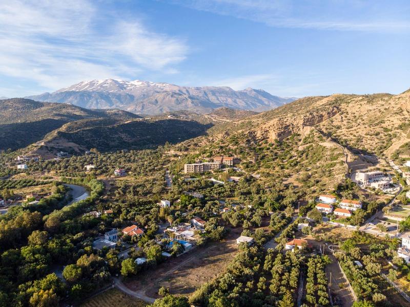 Paesaggio con valli verdi, case sparse e montagne innevate sullo sfondo.