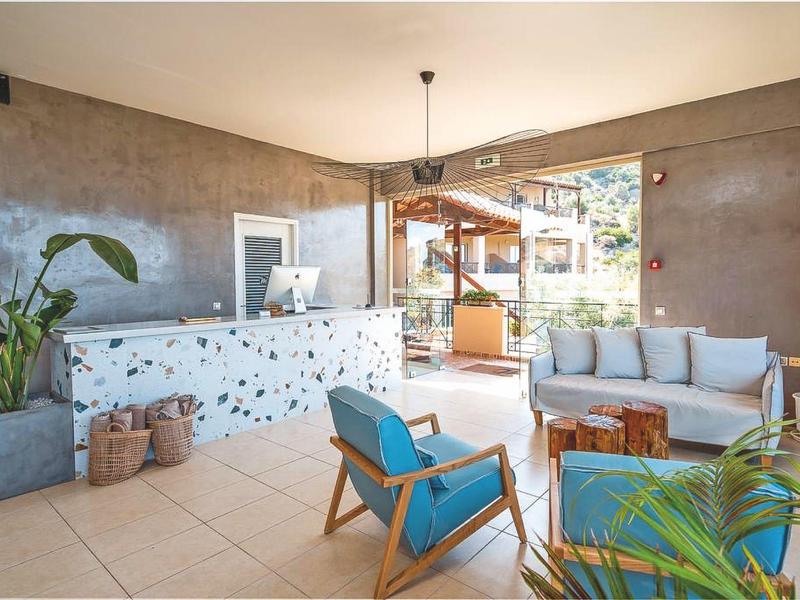 Sala d'ingresso dell'hotel luminosa con mobili moderni, poltrone blu e grandi finestre verso l'area esterna.