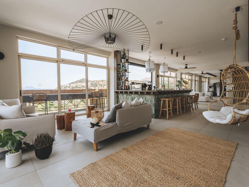 Interno di hotel luminoso e moderno con grandi finestre, aree salotto accoglienti e bar con vista.