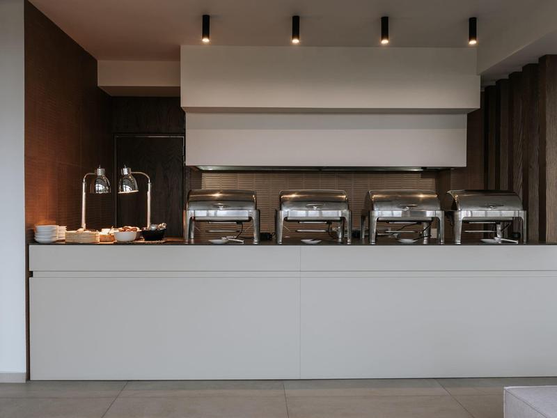 Stazione buffet con vassoi riscaldanti in acciaio inox e utensili da servizio in interni moderni.