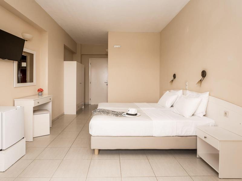 Camera d'albergo luminosa con letto grande, mobili bianchi e televisore a schermo piatto montato a parete.