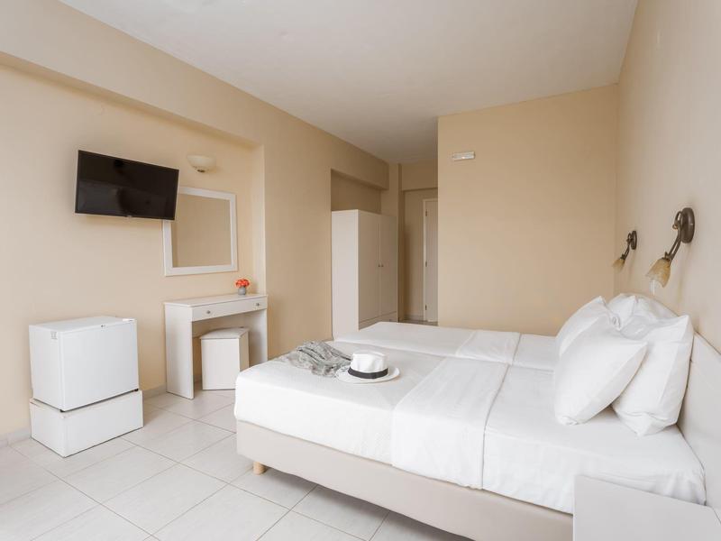 Camera d'albergo moderna con letto matrimoniale, TV a parete e mobili bianchi in tonalità neutre.