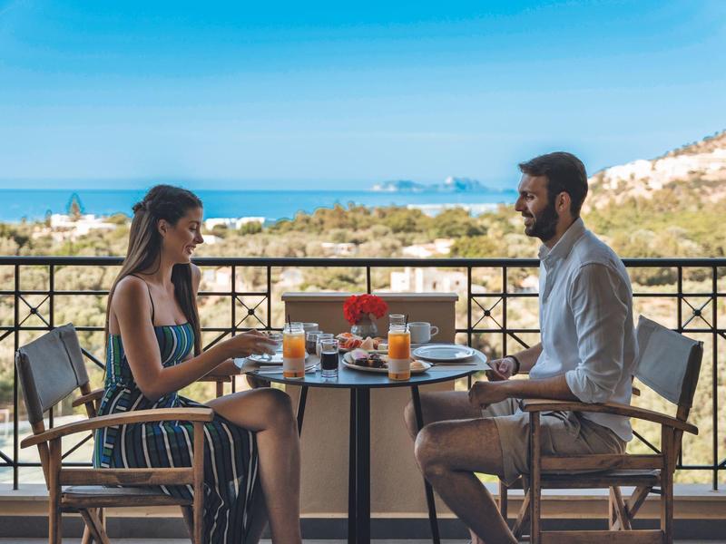 Coppia che fa colazione sul balcone con vista sul mare e le rocce