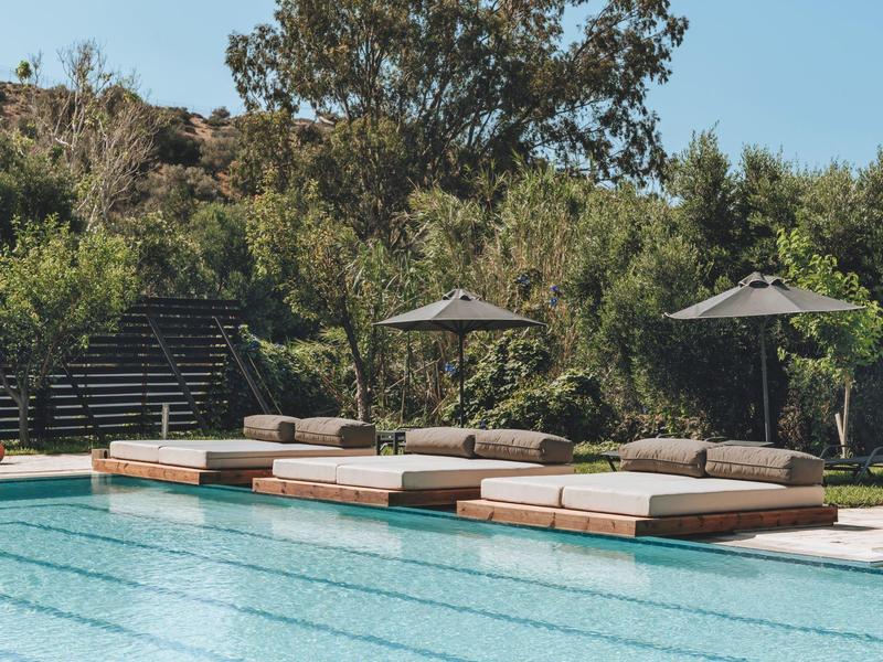 Area piscina con lettini e ombrelloni accanto a una piscina con acqua chiara e blu.