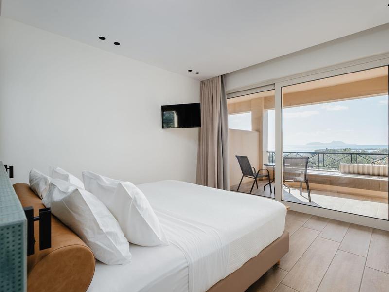 Camera d'hotel moderna con letto grande, finestre a tutta altezza, balcone con posti a sedere e vista mare.