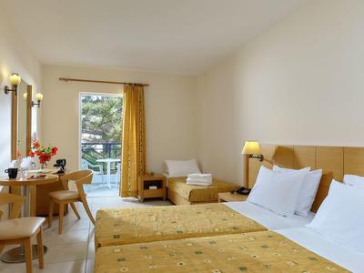 Camera d'hotel luminosa con due letti singoli, scrivania, sedie e vista sul balcone.